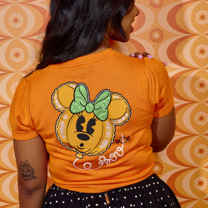 Woman wearing the orange Minnie Mouse Pumpkin Balloon Domonique Cardigan, facing away from the camera to show off the back where there is a design of a Minnie Mouse balloon and the string spells out "Boo"